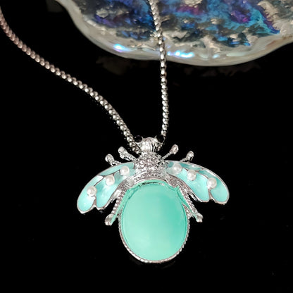 Collier pendentif insecte émail turquoise et perles nacrées — vue artistique sur fond noir avec cristal, détail finitions argentées - cadeau porte-bonheur