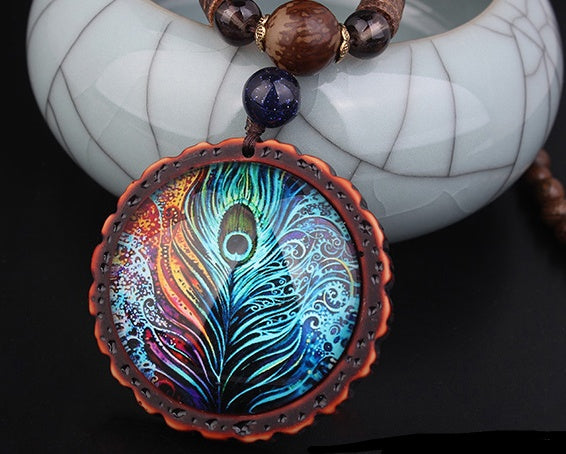 gros plan pendentif Gros plan sur le pendentif rond plume de paon irisé bleu turquoise et or – détail des reflets et de la monture