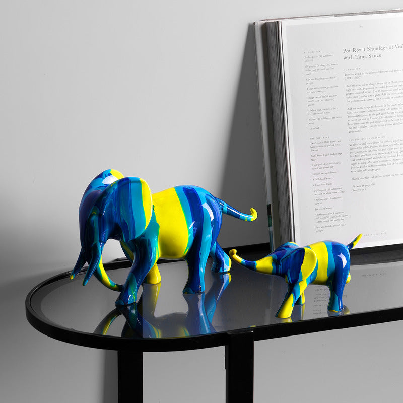 Duo mère et petit éléphant résine bleu jaune — petite trompe du petit tenant la queue de la mère, posés sur table console
