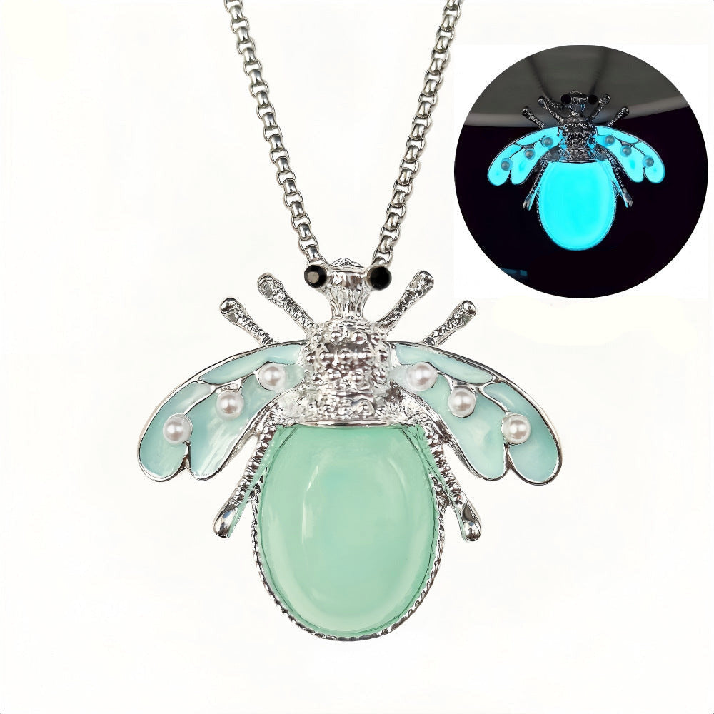Collier pendentif insecte phosphorescent bleu-vert — vue de face sur fond sombre, finitions argentées et perles nacrées, bijou lumineux nature - cadeau symbolique