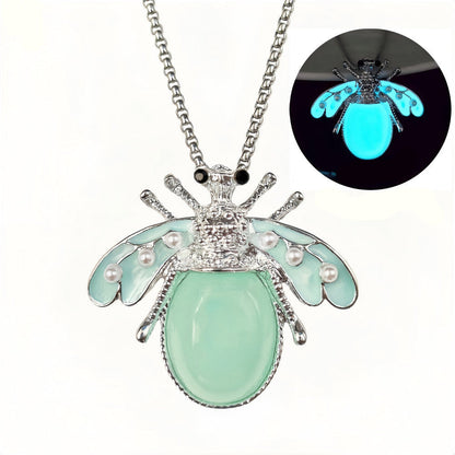 Collier pendentif insecte phosphorescent bleu-vert — vue de face sur fond sombre, finitions argentées et perles nacrées, bijou lumineux nature - cadeau symbolique